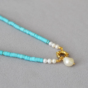 Macro shot of turquoise beads necklace featuring a white baroque pearl and gold ring clasp