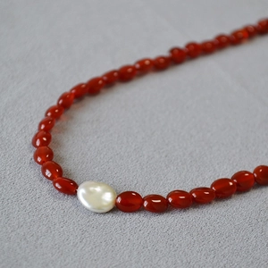 Détail du collier de perles baroques et agate rouge sur fond de tissu texturé gris