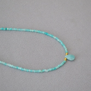 Macro detail of Amazonite beaded necklace with water drop pendant on gray fabric