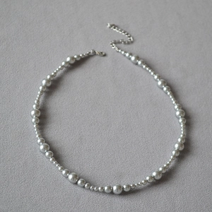 Detail of gray pearl beads necklace with silver adjustable chain on textured fabric