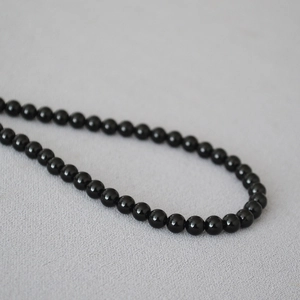 Dettaglio di collana con perle di onice nera lucida su sfondo di tessuto neutro