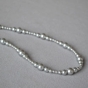 Detail of silver beaded necklace with varying sizes on textured gray fabric