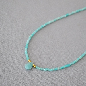 Minimalist turquoise beaded necklace with water drop stone pendant on grey fabric background