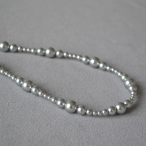 Detail of silver gray gradient pearl necklace with metallic luster on textured fabric