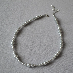 Detail of grey pearl gradient necklace with silver lobster clasp on grey fabric background