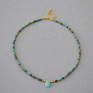 Detail of beaded necklace with turquoise stones and light blue water drop pendant