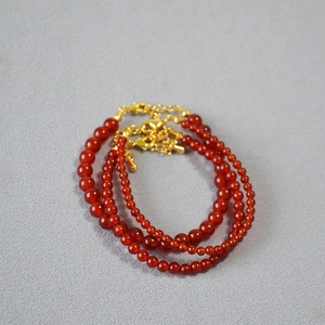 Close-up of red agate beaded bracelets with adjustable gold clasps on a textured base