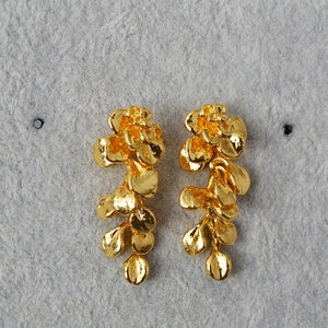Detailed view of gold flower tassel earrings with textured leaf pendants on grey felt