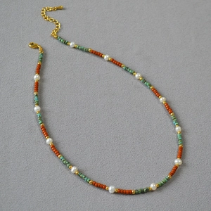 Minimalist freshwater pearl necklace with orange and turquoise beads on grey texture