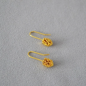 Close-up of golden pinecone pendant earrings with long U-shaped hooks on grey fabric
