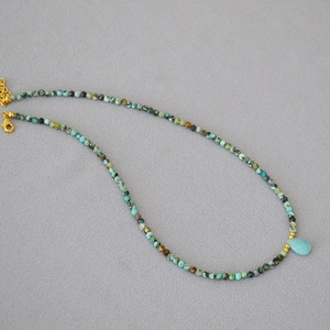 Detail of beaded stone necklace featuring a blue teardrop pendant and golden clasp