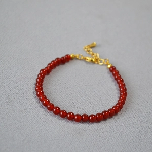 Detailed shot of red agate beaded bracelet with gold lobster clasp on grey fabric