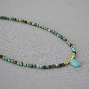 Detail of beaded necklace with turquoise stones, gold spacers, and a teardrop pendant