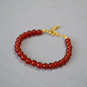 Close-up of deep red agate beaded bracelet with gold extension chain on gray background