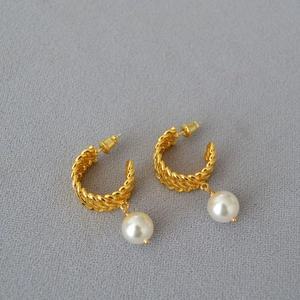 Detail of gold woven C-shape earrings with elegant round pearl pendants and studs