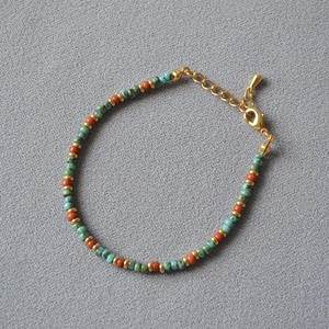 Gros plan d'un bracelet en perles avec détails verts et orange et fermoir mousqueton