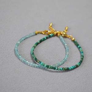 Detail of stacked minimalist bracelets with blue and turquoise beads and golden clasps