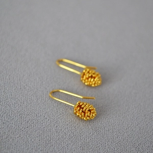 Detailed close-up of golden pinecone earrings with textured finish on gray fabric