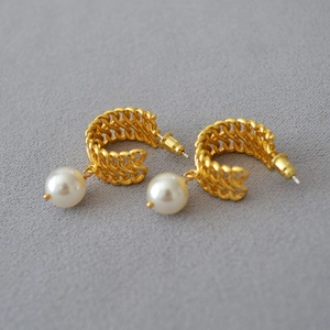 Detailed view of woven golden C-shaped stud earrings featuring elegant hanging white pearls