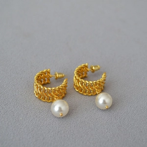 Macro shot of gold-plated woven metal C-shape earring featuring a lustrous white pearl