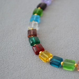 Macro shot of colorful translucent square beads with golden spacers on a fabric background