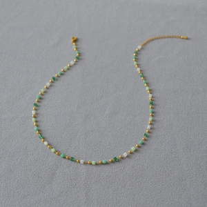Elegant beaded necklace with gradient green beads and gold accents on gray background