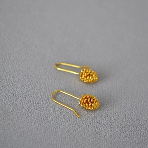Macro detail of gold-plated pine cone earrings with intricate scale texture on dark fabric