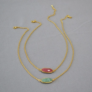 Close-up of gold-plated necklaces with pink and green faceted oval natural stones