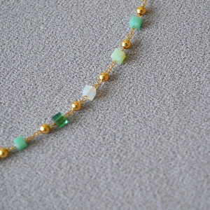 Macro detail of minimalist gold necklace featuring green and white cubic beads on a fine chain