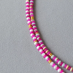 Gros plan sur un collier de perles colorées avec détails rose vif et métal doré