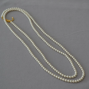 Détail d'un collier de perles rondes avec fermoir mousqueton doré et chaîne réglable