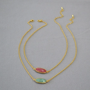 Detail of two gold plated brass necklaces with pink and green faceted gemstones