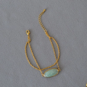 Dettaglio del bracciale a catena dorata con pietra verde ovale e chiusura a moschettone
