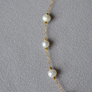 Detail of three white pearls and gold beads on a fine chain over grey textured fabric