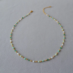 Detail of beaded necklace with green and white square beads and gold-tone spacers