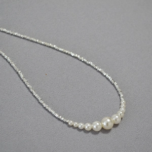Close-up of irregular silver-tone metal chain with gradient faux pearls on grey fabric