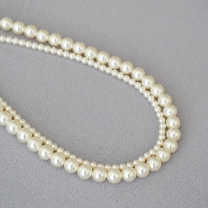 Detail of double-layer faux pearl necklace with ivory beads on textured grey background