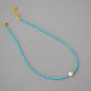 Detailed view of turquoise beaded necklace with baroque pearl and golden lobster clasp