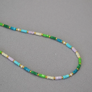 Collana di perline turchesi colorate con accenti dorati e perle su tessuto grigio