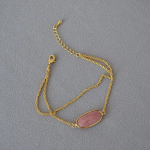Dettaglio di una pietra naturale rosa su un bracciale a doppia catena dorata con moschettone