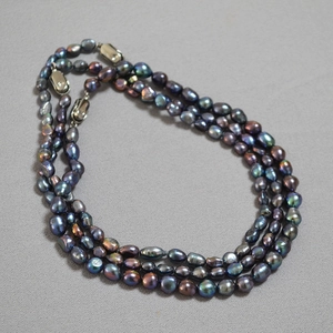 Detailed view of triple-strand baroque pearl necklace with peacock green metallic luster
