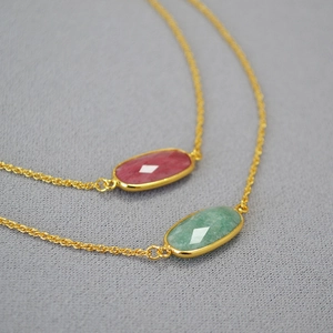 Macro shot of minimalist gold chain necklaces featuring rose red and green oval gemstones