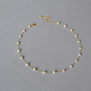 Detail of elegant gold-plated brass necklace with white baroque pearls on dark background