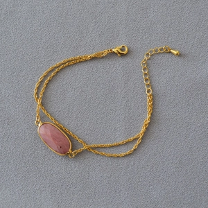 Dettaglio del bracciale a doppia catena dorata con pietra rosa e chiusura regolabile