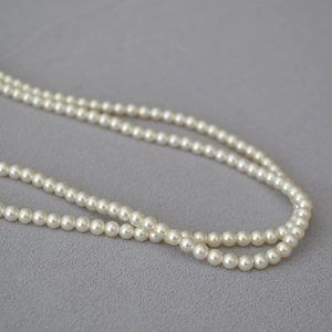 Gros plan sur un collier de perles crème élégant sur un tissu texturé gris minimaliste