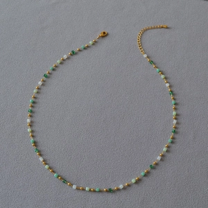 Elegant beaded necklace with gradient green cubes and gold beads on grey background