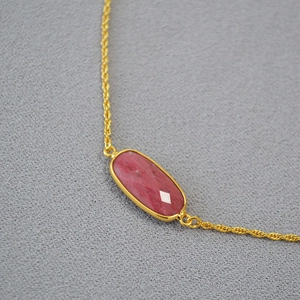 Detail shot of a gold-plated brass necklace with a natural red gemstone pendant