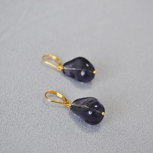 Detail of drop earrings with deep purple irregular glass and golden metal hooks