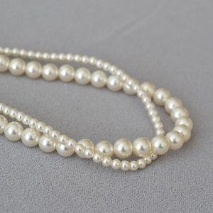 Detailed close-up of a double-layered pearl necklace with cream white beads on grey fabric