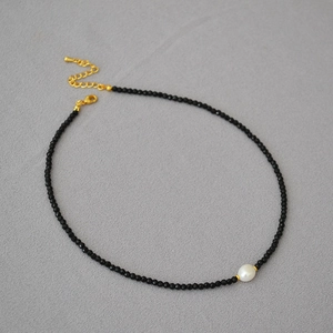 Macro detail of handmade black spinel beads and a baroque pearl on a gold clasp necklace